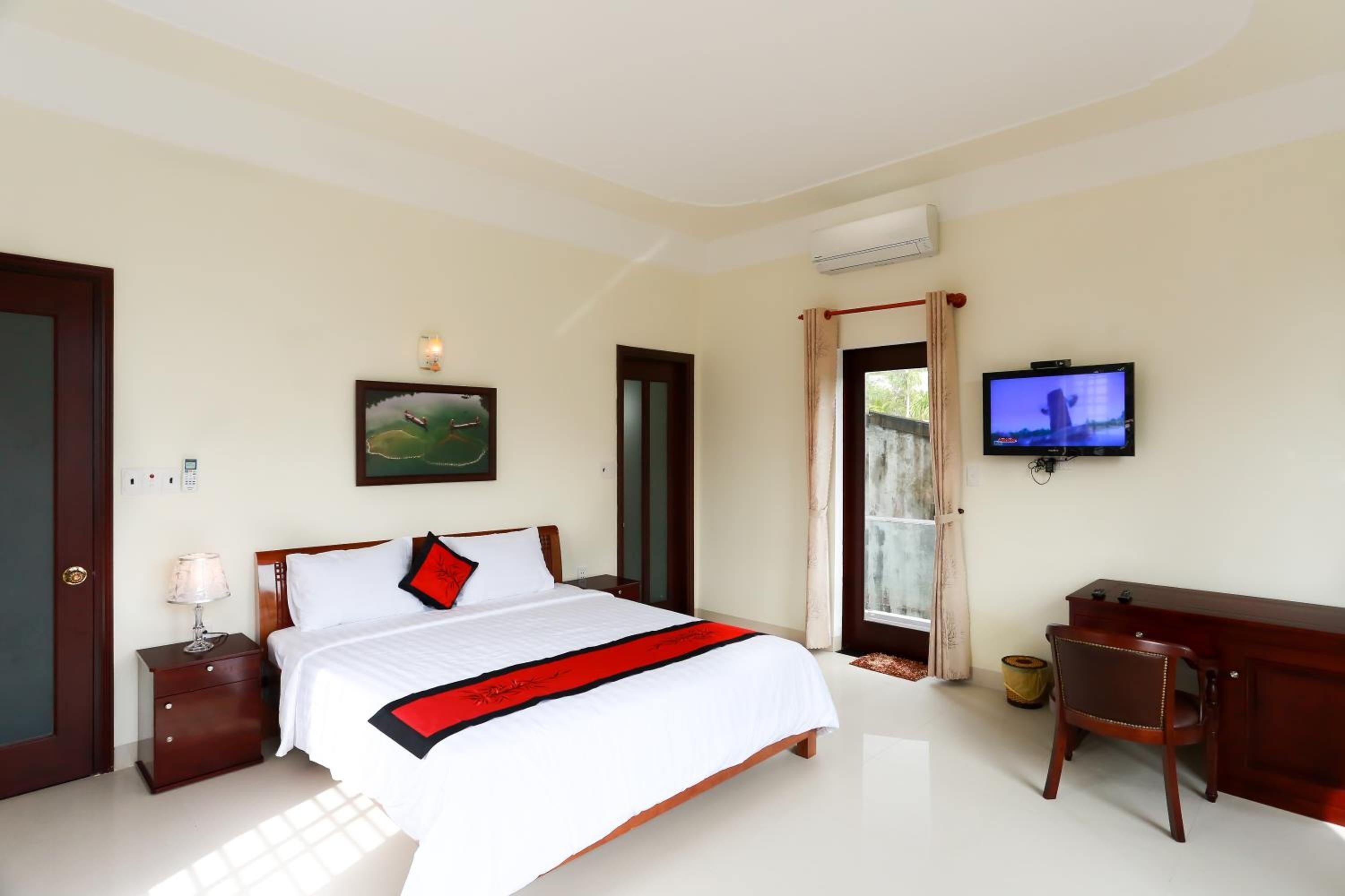 A hotel bedroom with a bed, a desk, a television, and a painting on the wall.