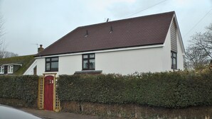 Ein zweistöckiges Haus mit roter Tür, weißen Wänden und einem braunen Dach.