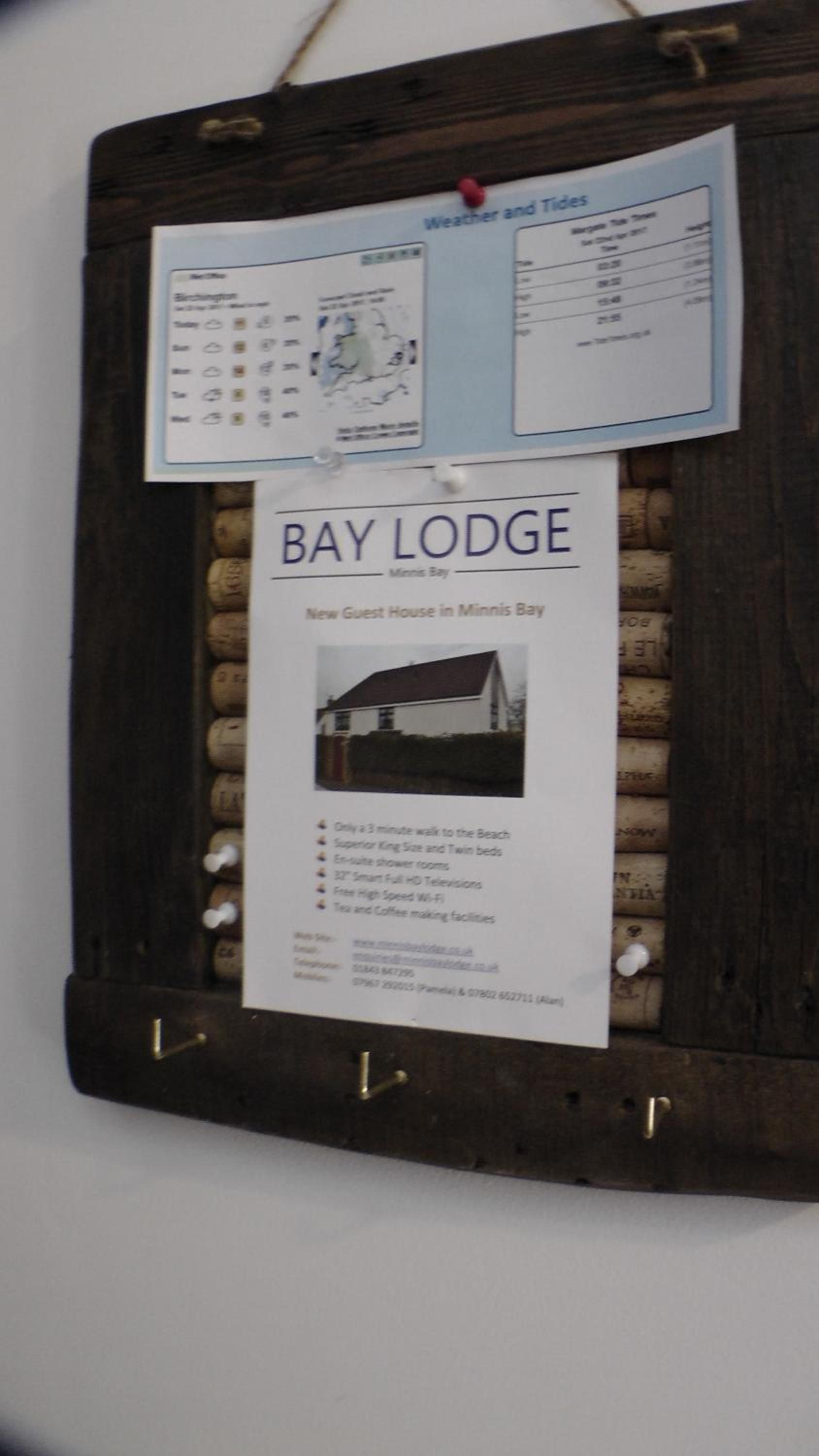 Un tablón de anuncios con un listado de Bay Lodge, que incluye comodidades como a 3 minutos caminando de la playa, camas extragrandes de lujo, baños privados con ducha, televisores inteligentes de alta definición, Wi-Fi gratuito de alta velocidad y set de té y café.