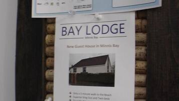 Un tablón de anuncios con un listado de Bay Lodge, que incluye comodidades como a 3 minutos caminando de la playa, camas extragrandes de lujo, baños privados con ducha, televisores inteligentes de alta definición, Wi-Fi gratuito de alta velocidad y set de té y café.