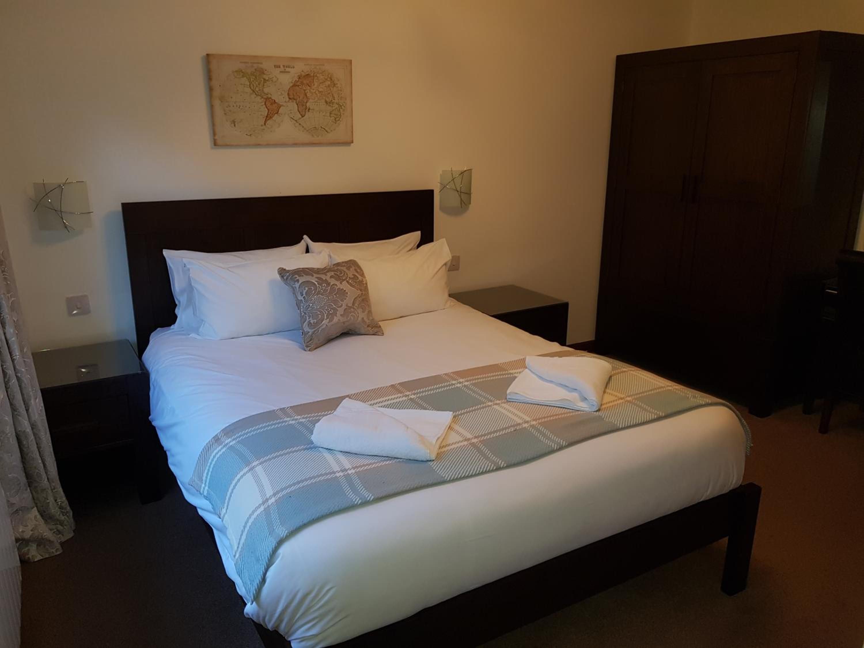 A neatly made bed with a plaid bedspread, a pillow, and a folded towel on the side.