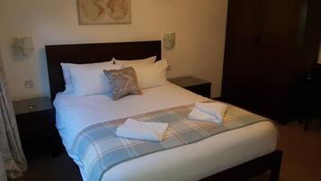 A neatly made bed with a plaid bedspread, a pillow, and a folded towel on the side.