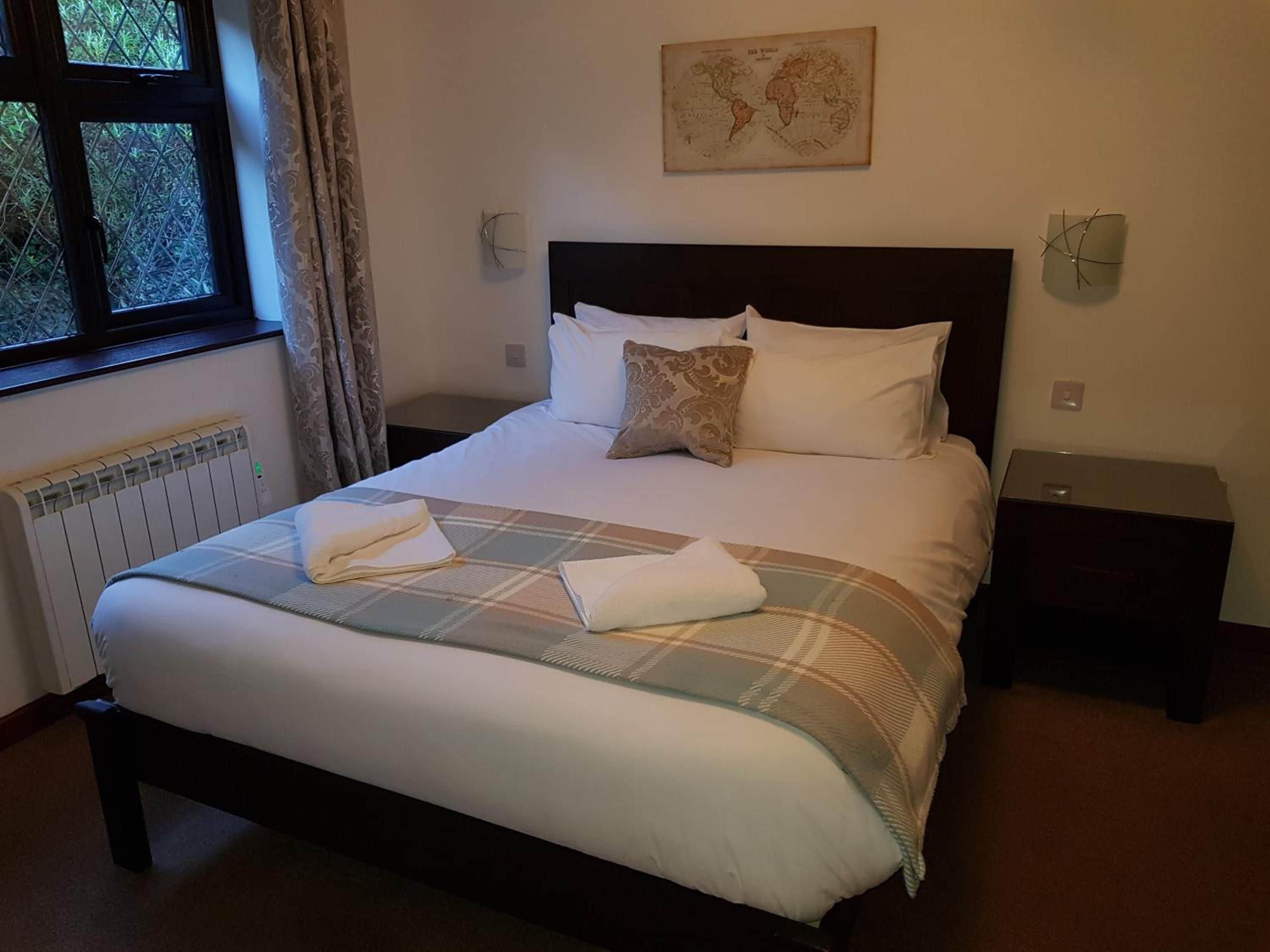 A neatly made bed with a plaid bedspread and pillows, a world map on the wall, and a window with curtains.