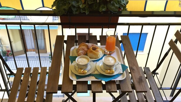 A balcony with a wooden table set with croissants, coffee cups, and a glass of orange juice, under a yellow striped awning. - Il Saraceno (Sorrento)