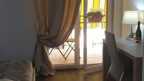 A hotel room with a bed, a desk with a lamp, a chair, and a view through a window with curtains. - Il Saraceno (Sorrento)