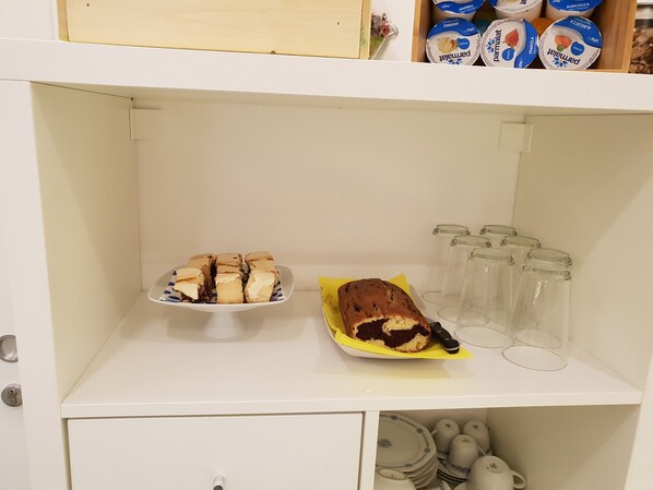 A white cabinet with a plate of pastries, a loaf of bread, and several glass jars.