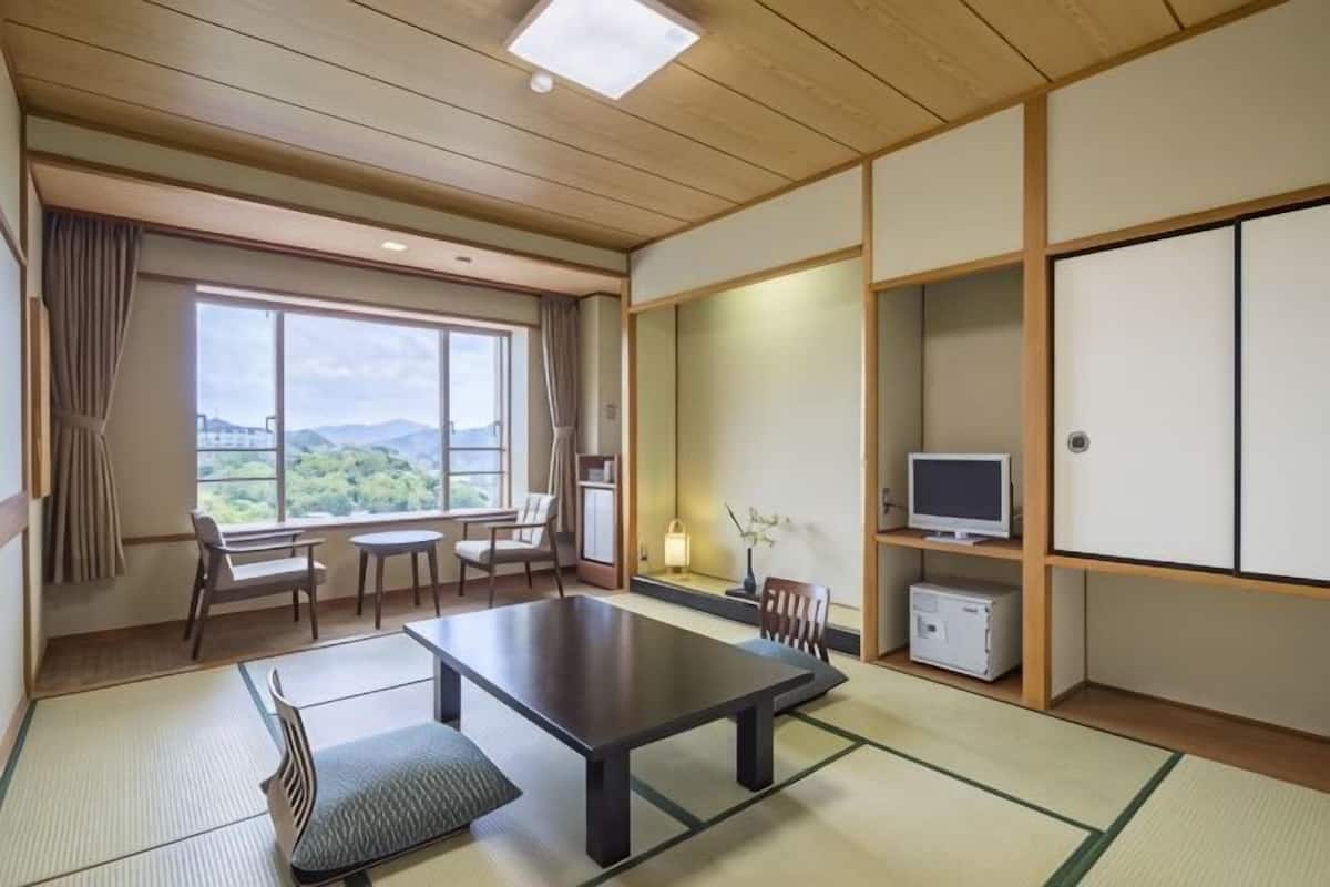 A traditional Japanese room with tatami flooring, a low table, a TV, and a view of the outdoors.