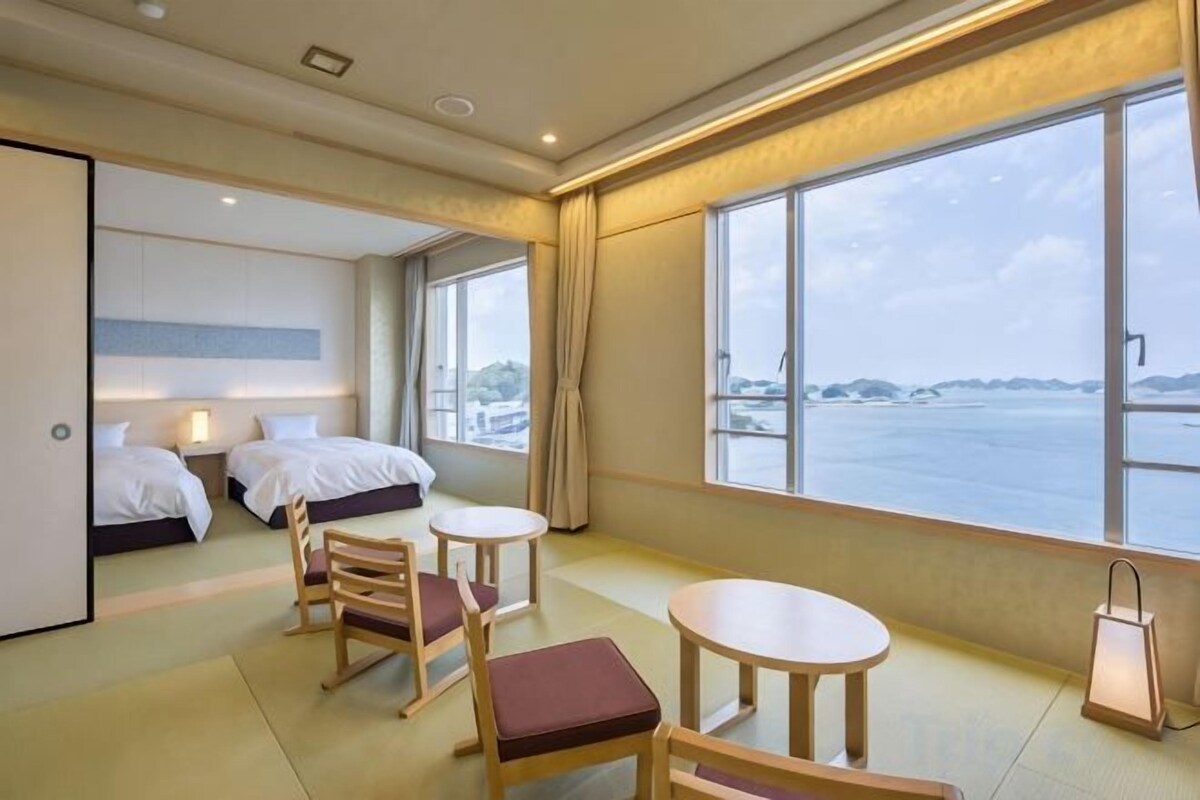 Habitación de hotel con dos camas, una mesa de comedor, sillas, una mesita y vistas al mar.