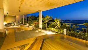 A wooden deck with a hot tub and seating area overlooking a body of water at night. - Toba Seaside Hotel (Toba)