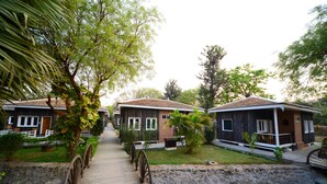 A pathway leading to a row of rustic-style cabins with a stone wall and a wooden bridge. - KMA Bagan Village Hotel (Nyaung-U)