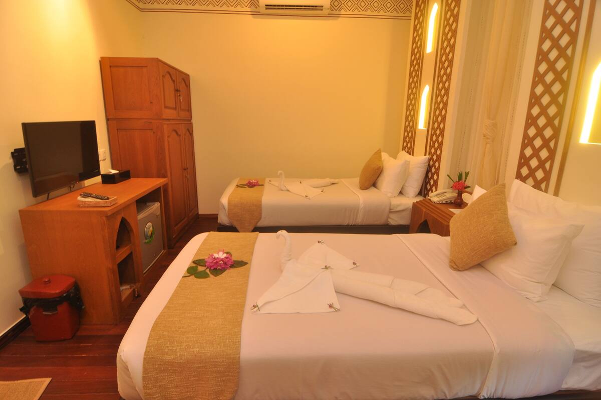 A hotel room with two beds, a television, a wooden cabinet, and a small trash bin.