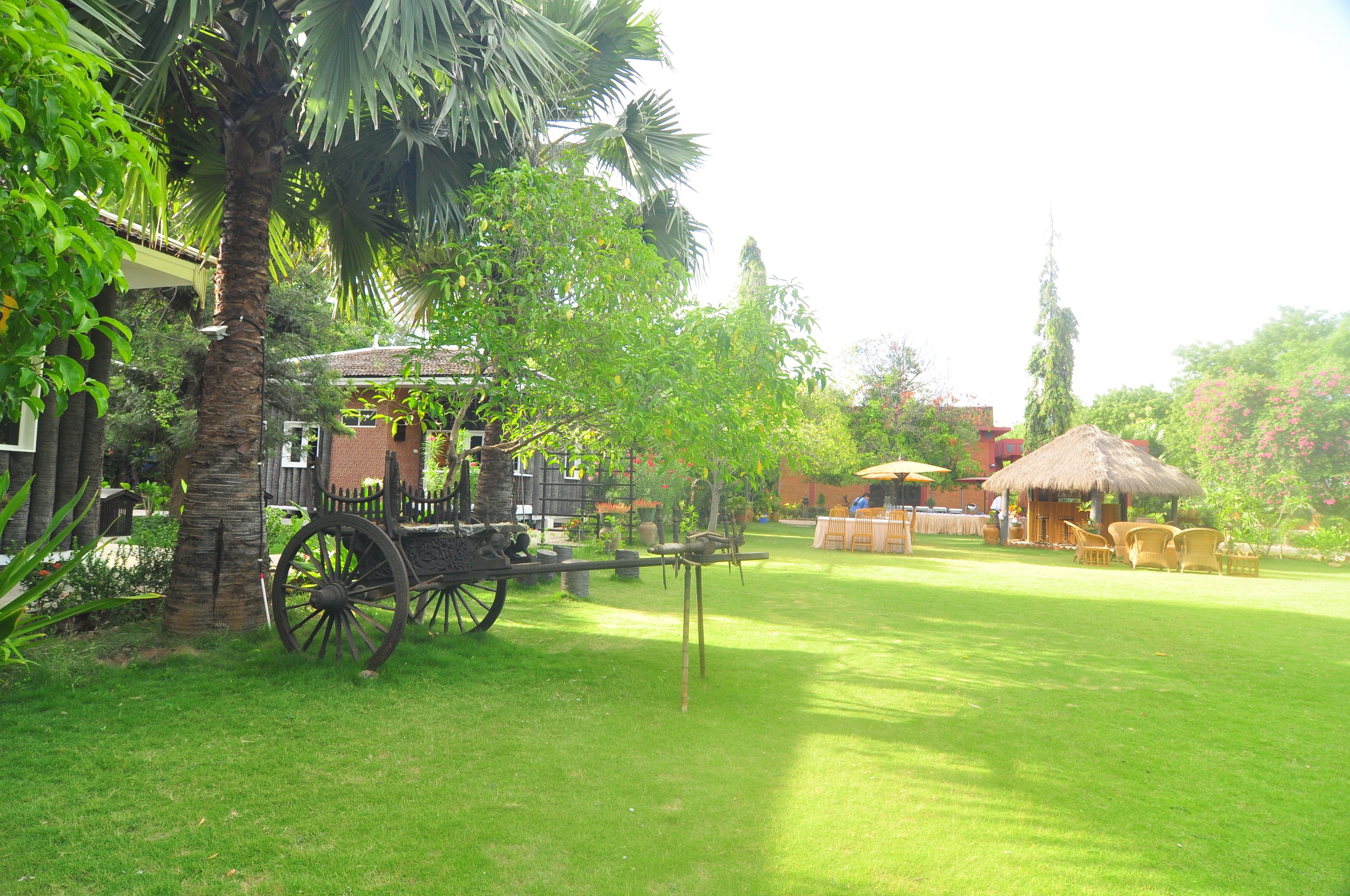 Um jardim exuberante com uma carruagem antiga, uma construção com telhado de palha e mobiliário de exterior.