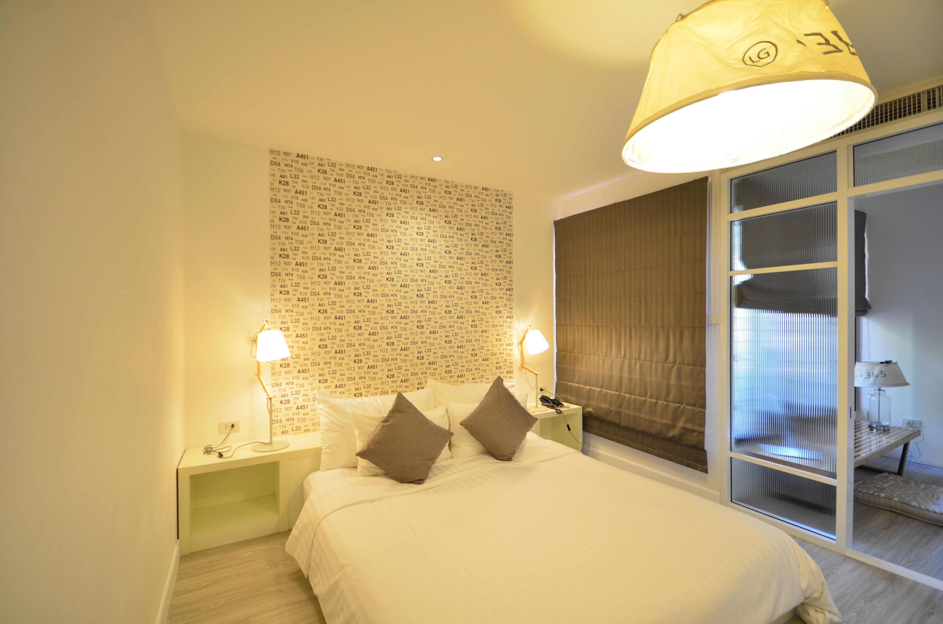 A hotel room with a large bed, two bedside lamps, a wall with text, and a window with curtains.