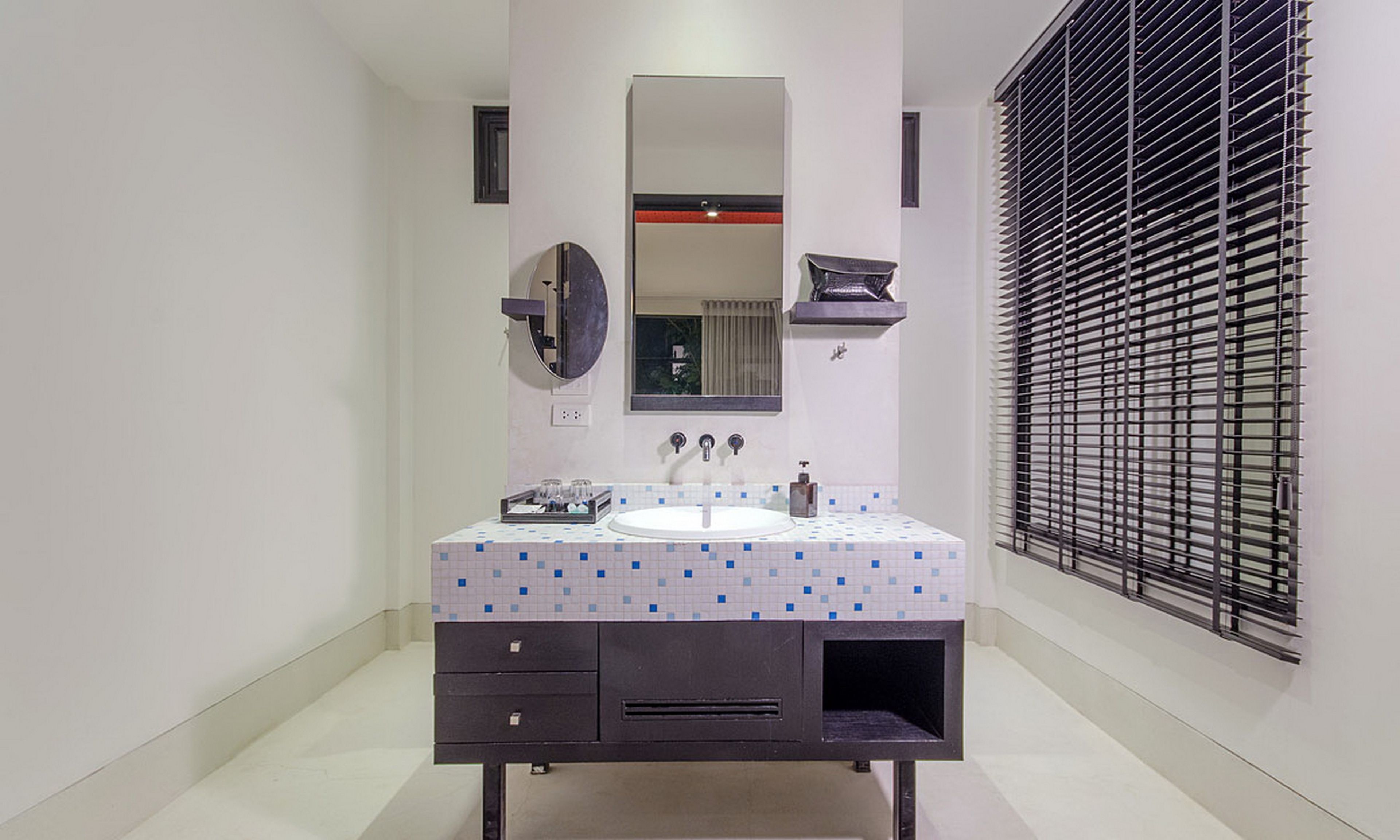 A bathroom with a white sink, dark vanity, and a large mirror. There is a window with blinds on the right.