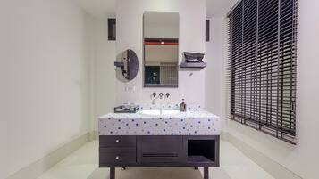 A bathroom with a white sink, dark vanity, and a large mirror. There is a window with blinds on the right.