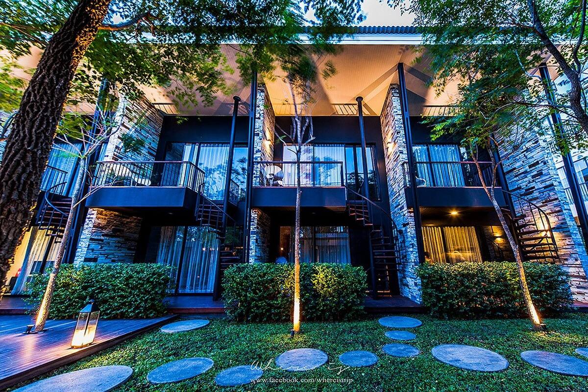A modern multi-story building with balconies, a central staircase, and a well-maintained garden with stone pathways.