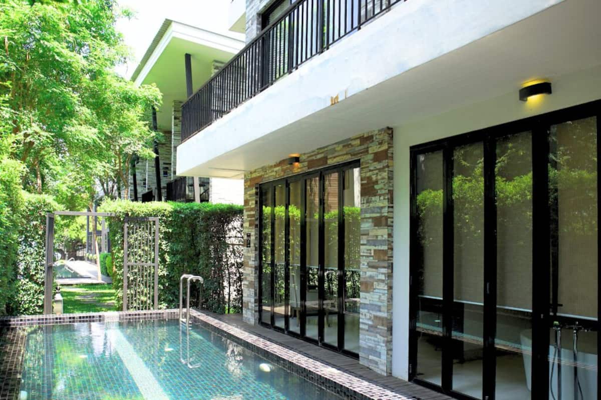 A modern outdoor swimming pool with a stone facade, glass doors, and a balcony overlooking the pool.