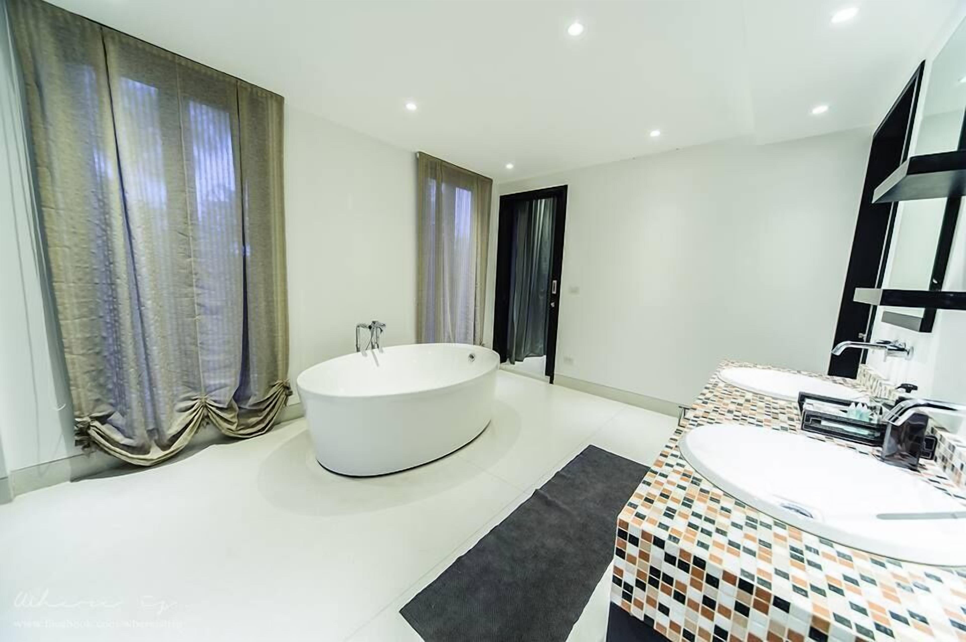 Un baño moderno con una bañera independiente, dos lavamanos y un espejo grande.