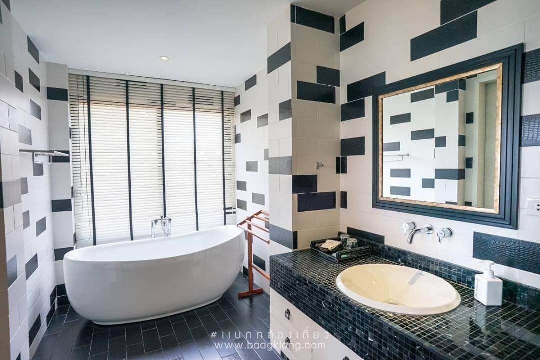 A modern bathroom with a freestanding bathtub, a large mirror, and a black and white tiled backsplash.