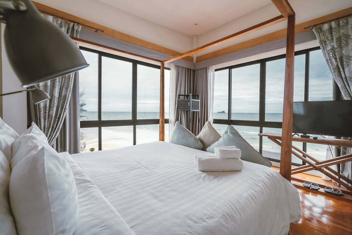A hotel room with a large bed, a TV, and a view of the sea.