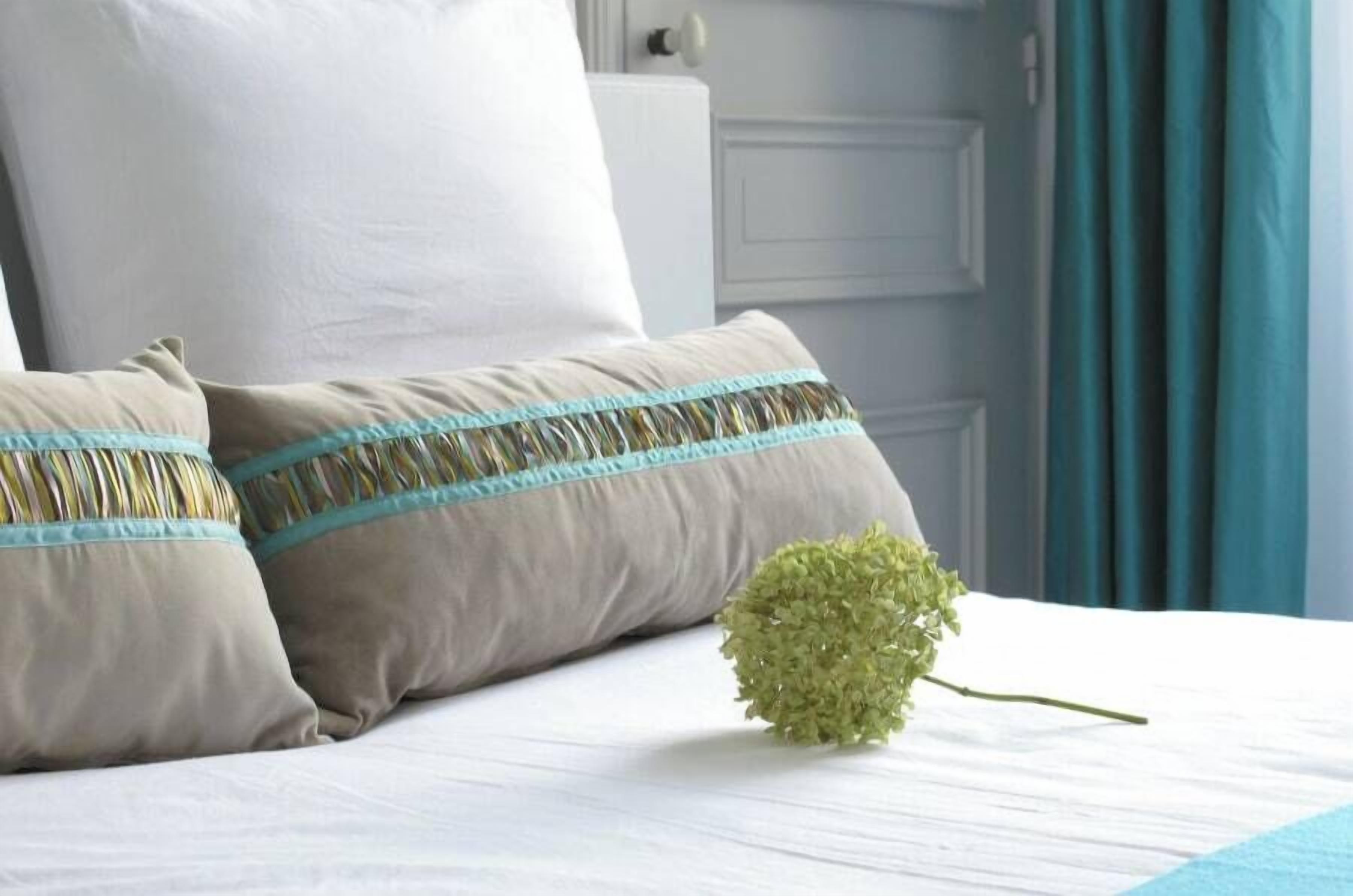 Ein ordentlich bezogenes Bett mit zwei Kissen und einer einzelnen grünen Hortensie darauf.