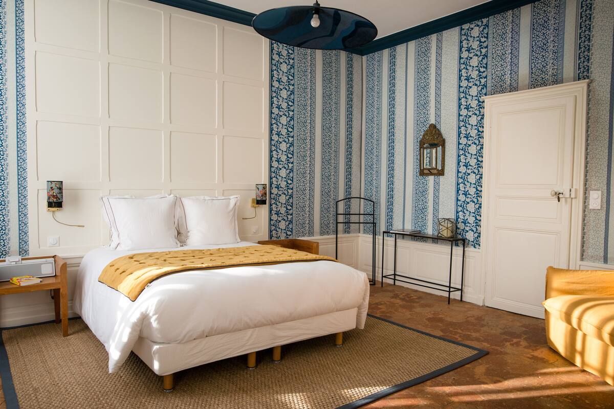 Un dormitorio ordenado con cama, mesita de noche, lámpara y una puerta.