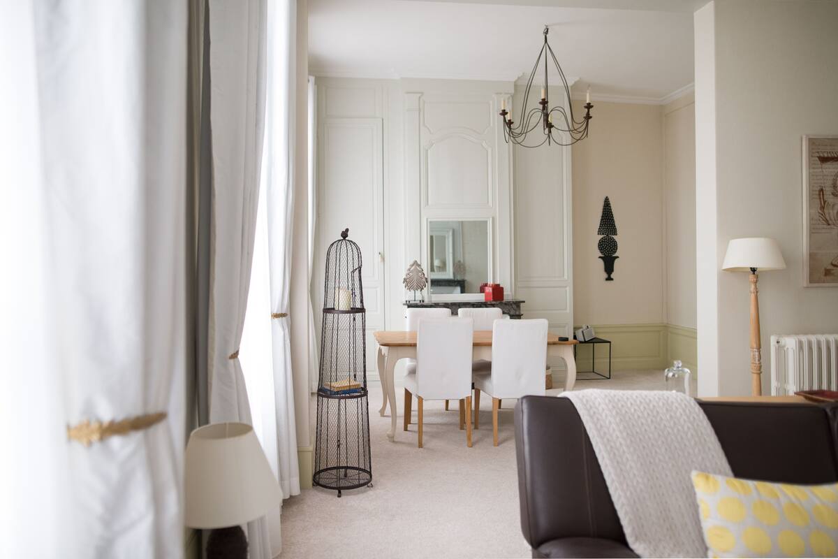 Una sala de estar moderna con comedor, muebles blancos, una araña y una jaula de pájaros.