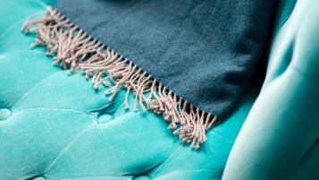 A close-up of a teal upholstered sofa with a dark blanket draped over it.