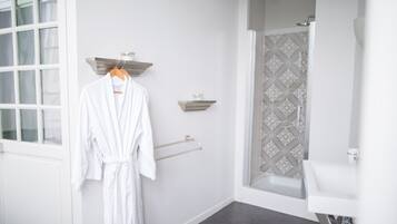A bathroom with a white bathtub, a shower with patterned tiles, a white sink, and a robe hanging on a rack.