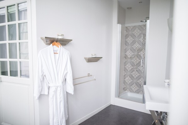 A bathroom with a white bathtub, a shower with patterned tiles, a white sink, and a robe hanging on a rack.