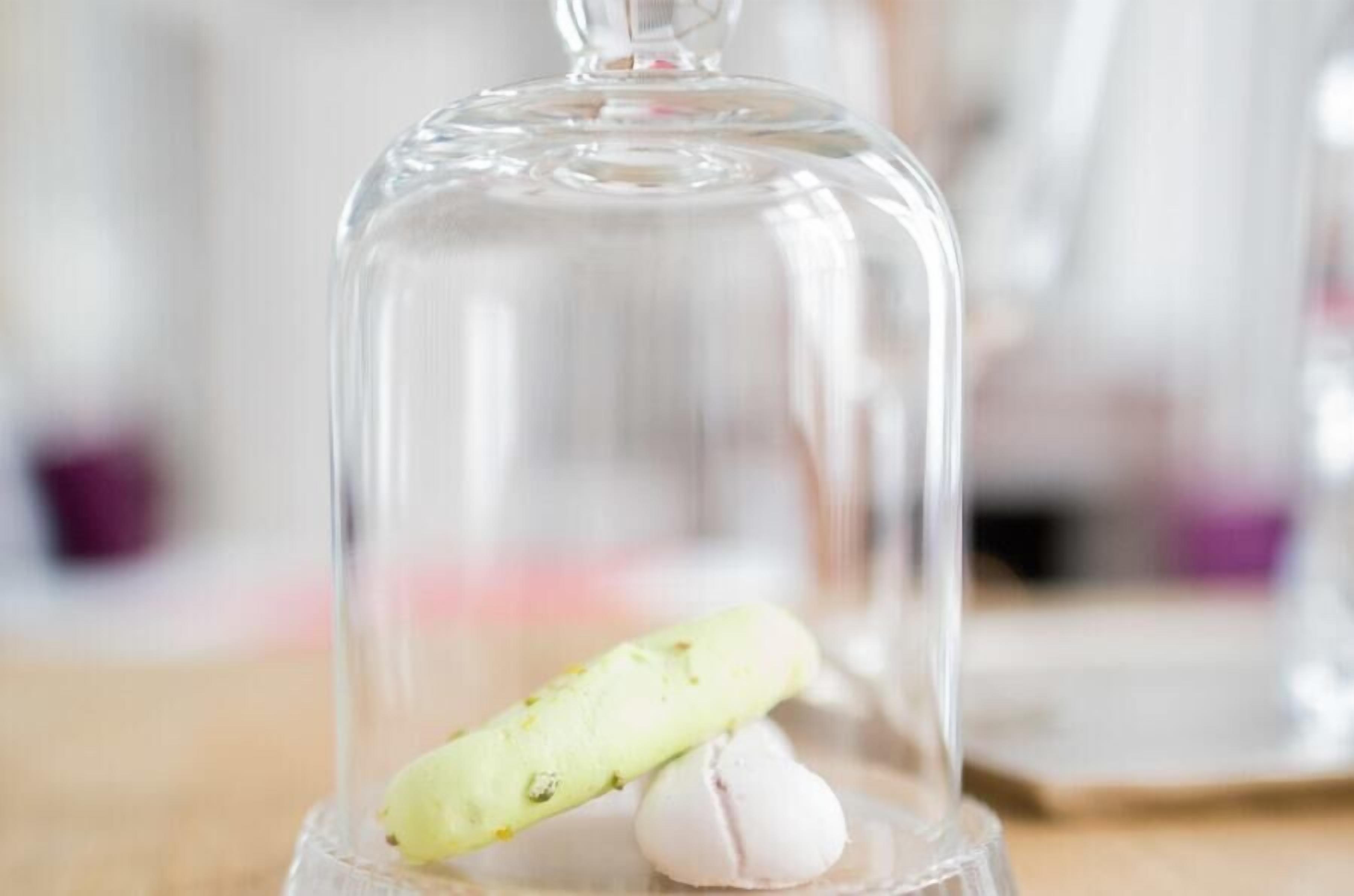 A clear glass dome over a table with a green object and a white object inside.