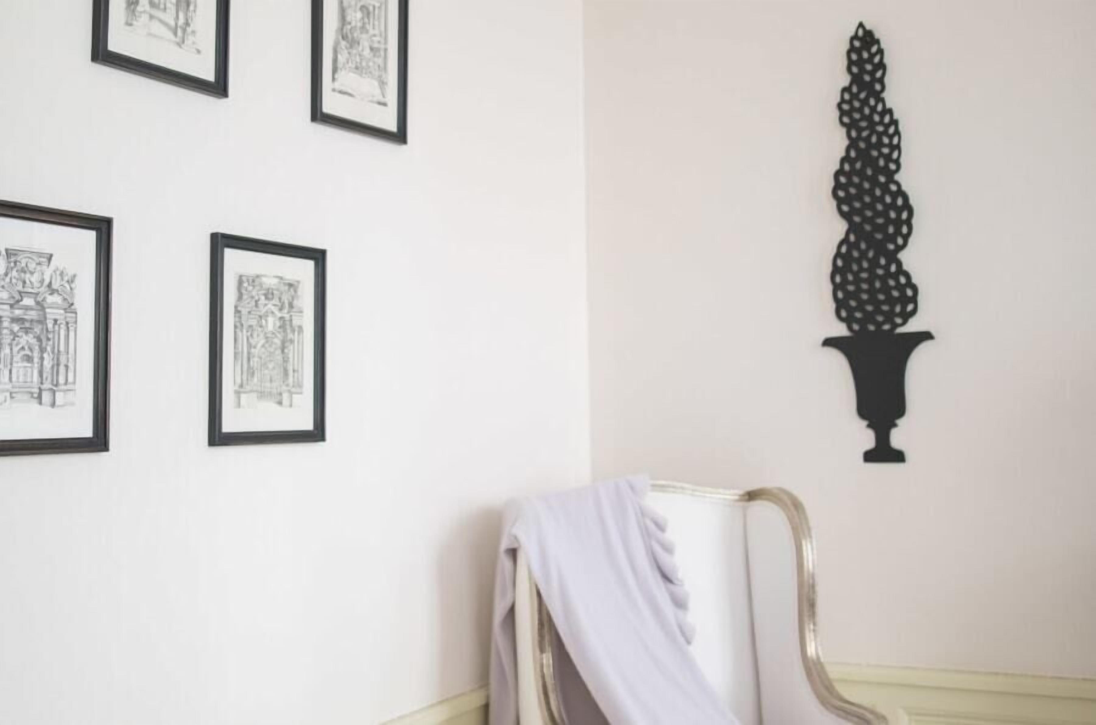 Een kamer met lijstwerken aan de muur, een stoel met een draperende stof en een decoratieve zwarte vaas.