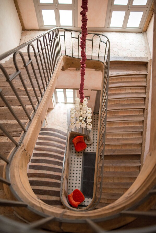 A spiral staircase with a wooden handrail and metal balusters, leading to a landing with a red decorative element and a series of white spherical objects.