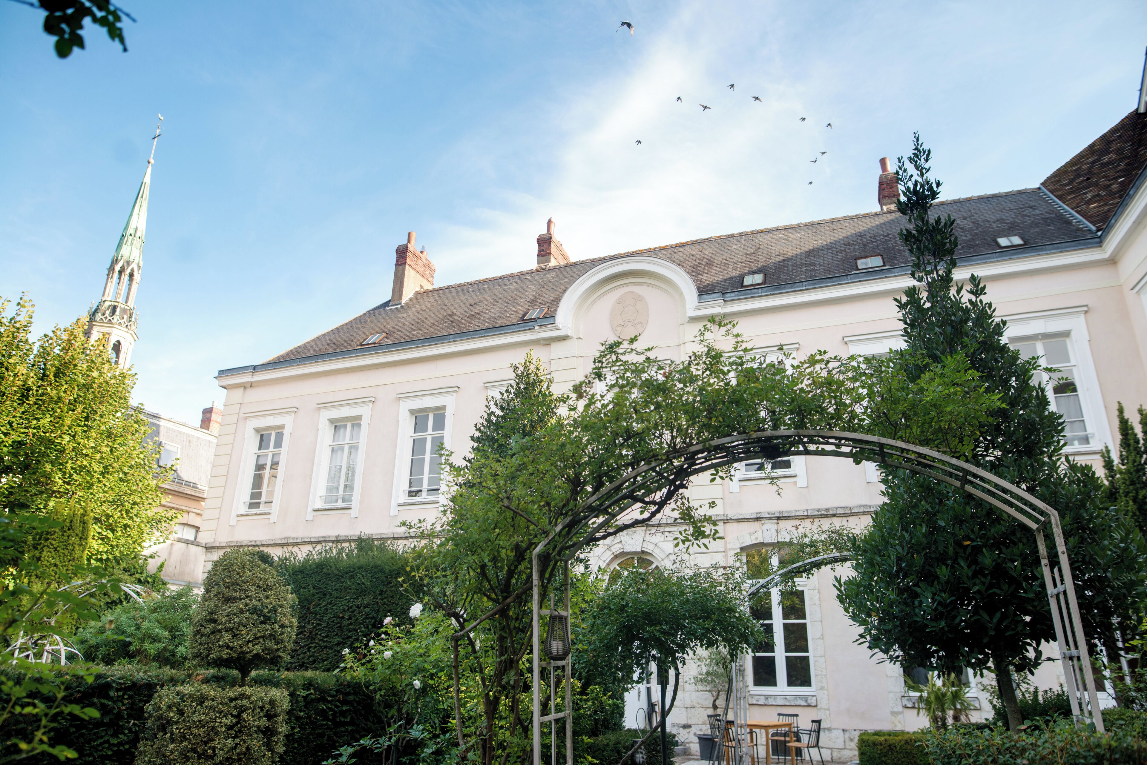 A historic building with a garden, a white facade, and a traditional roof.