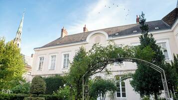 A historic building with a garden, a white facade, and a traditional roof.