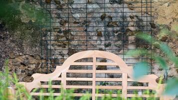 Un banco de madera con respaldo de rejilla, situado frente a un muro de piedra con diseño de cuadrícula.