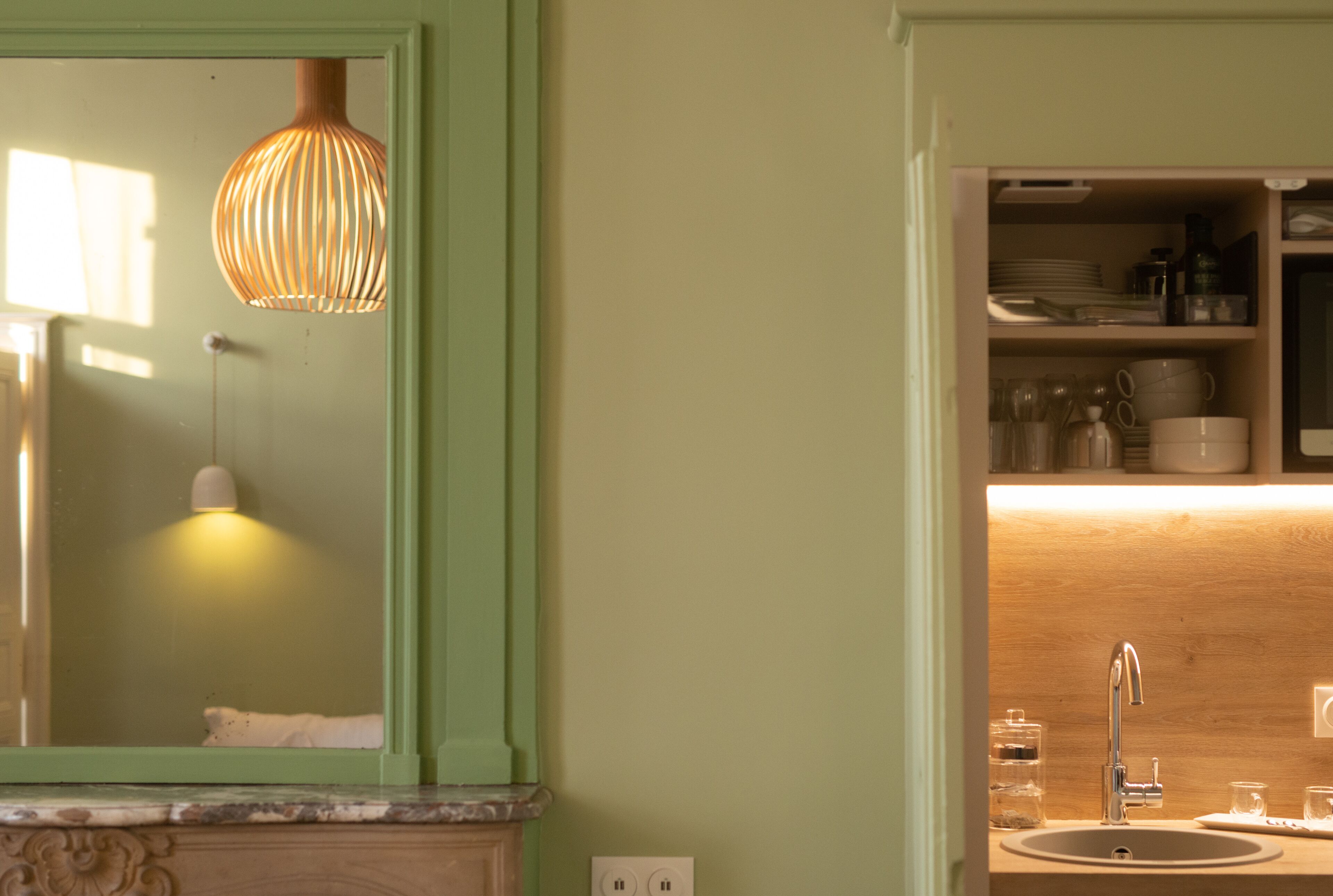 A bathroom with a large mirror, a hanging light fixture, a sink, and shelves with toiletries.