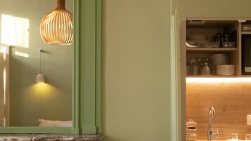 A bathroom with a large mirror, a hanging light fixture, a sink, and shelves with toiletries.