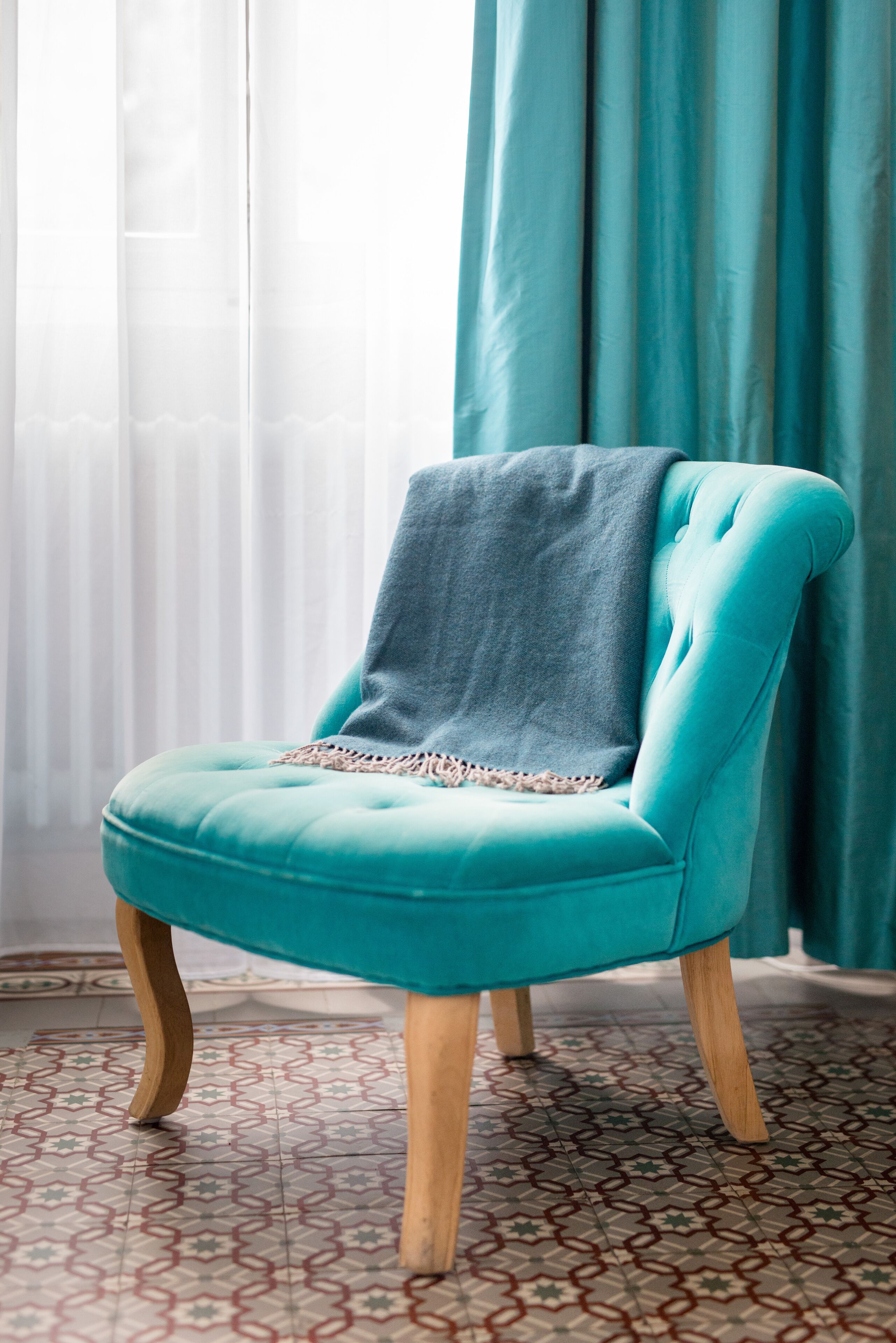 Un sillón azul aguamarina con una manta gris, patas de madera y un suelo estampado.