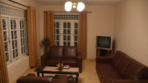Una sala de estar con un sofá de cuero marrón, una mesa de centro con un objeto decorativo, un televisor sobre un mueble bajo y una ventana con cortinas.
