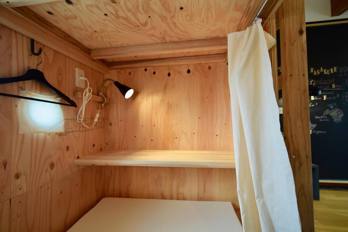 Een houten kamer met een bed, een hanglamp, een zwarte ophanger en een wit gordijn.