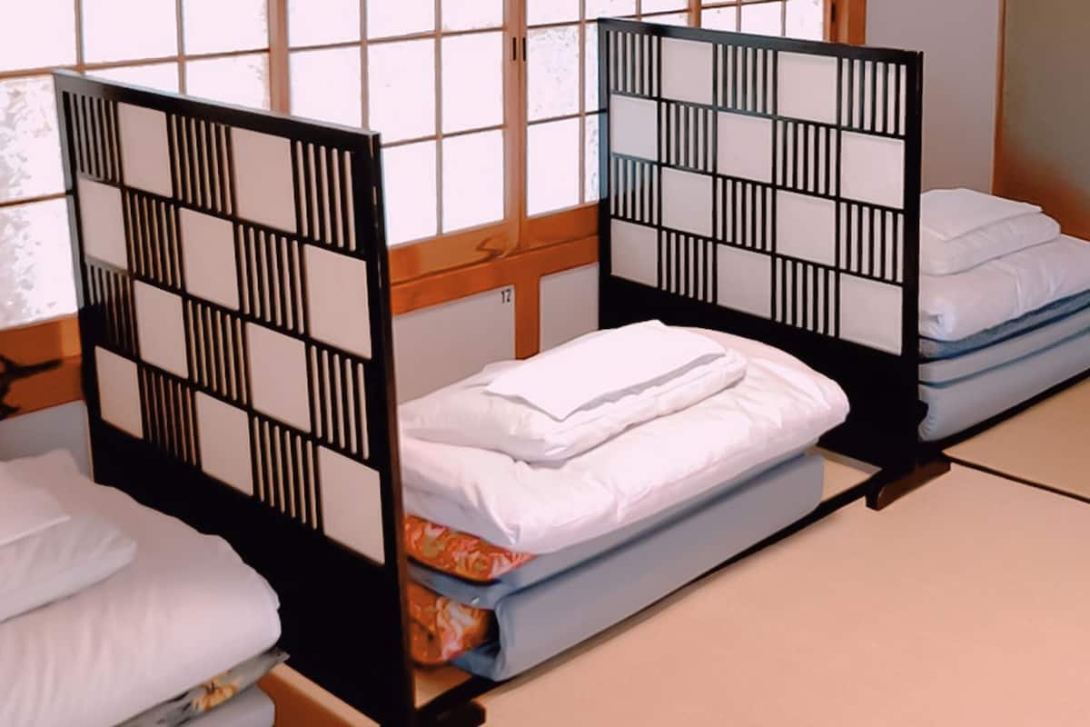 Een traditionele Japanse kamer met tatami vloeren en lage houten bedden met zwarte frames en witte beddengoed.