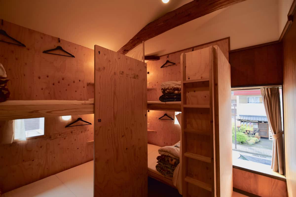Een kamer met een stapelbed, houten planken en een raam met gordijnen.
