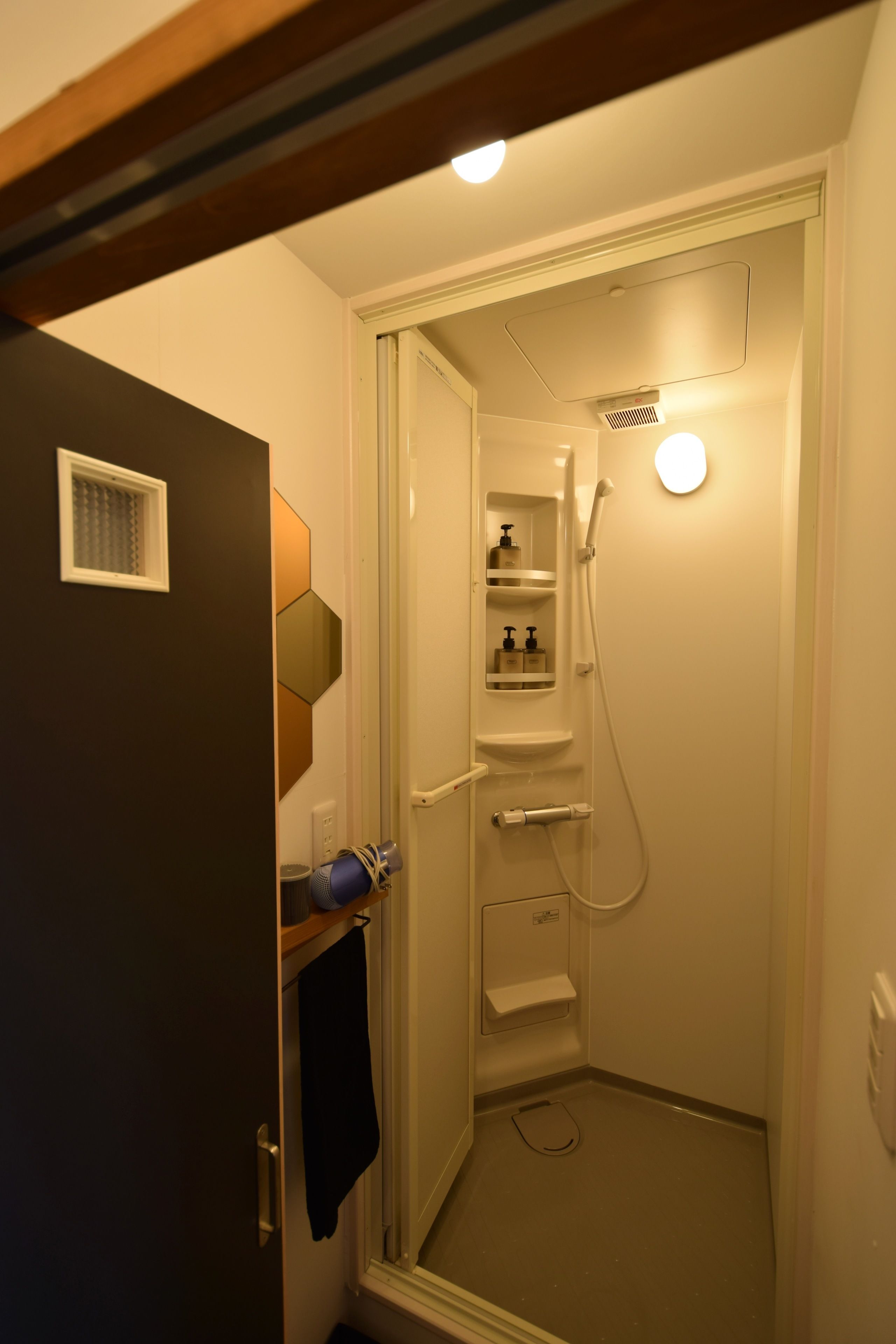 Un espacio de ducha pequeño y cerrado con puerta de vidrio, una toalla colgada en la puerta y un estante con artículos de aseo.