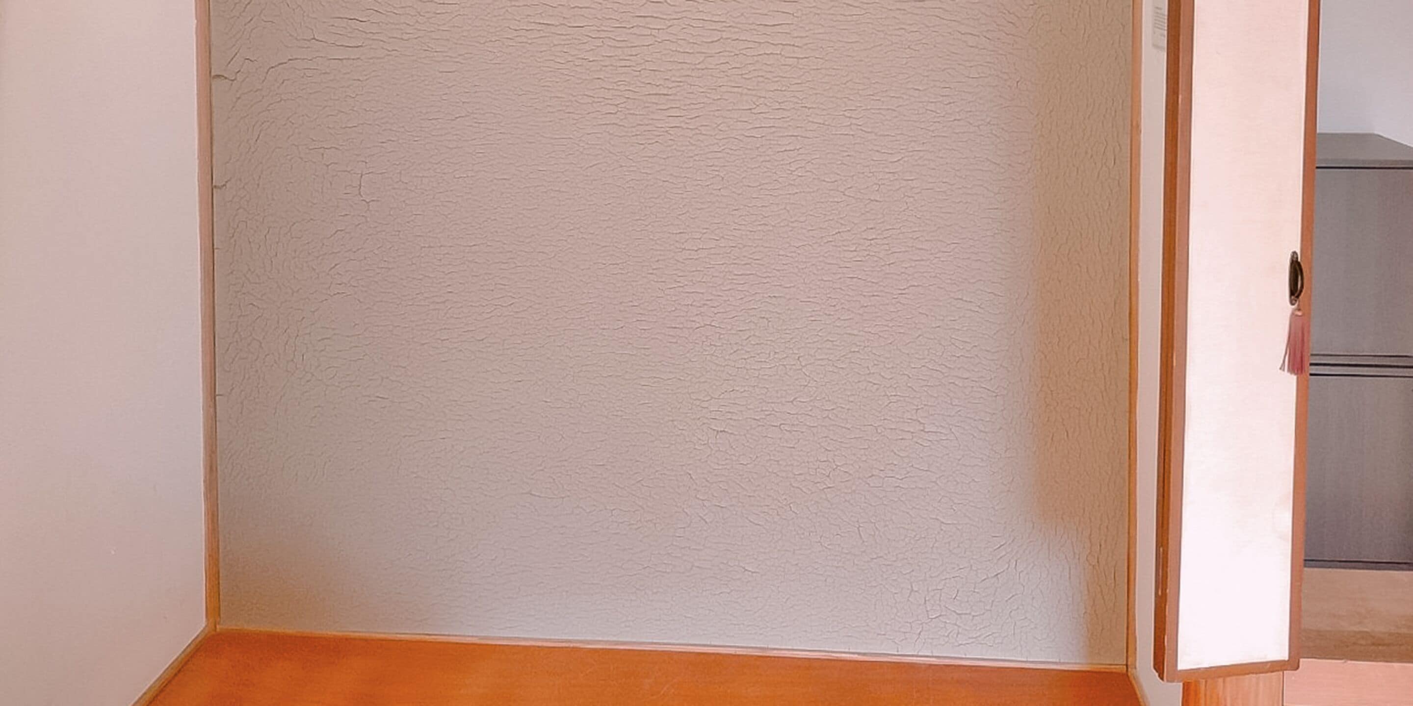 Una esquina de una habitación con una pared blanca texturizada y un suelo de madera.