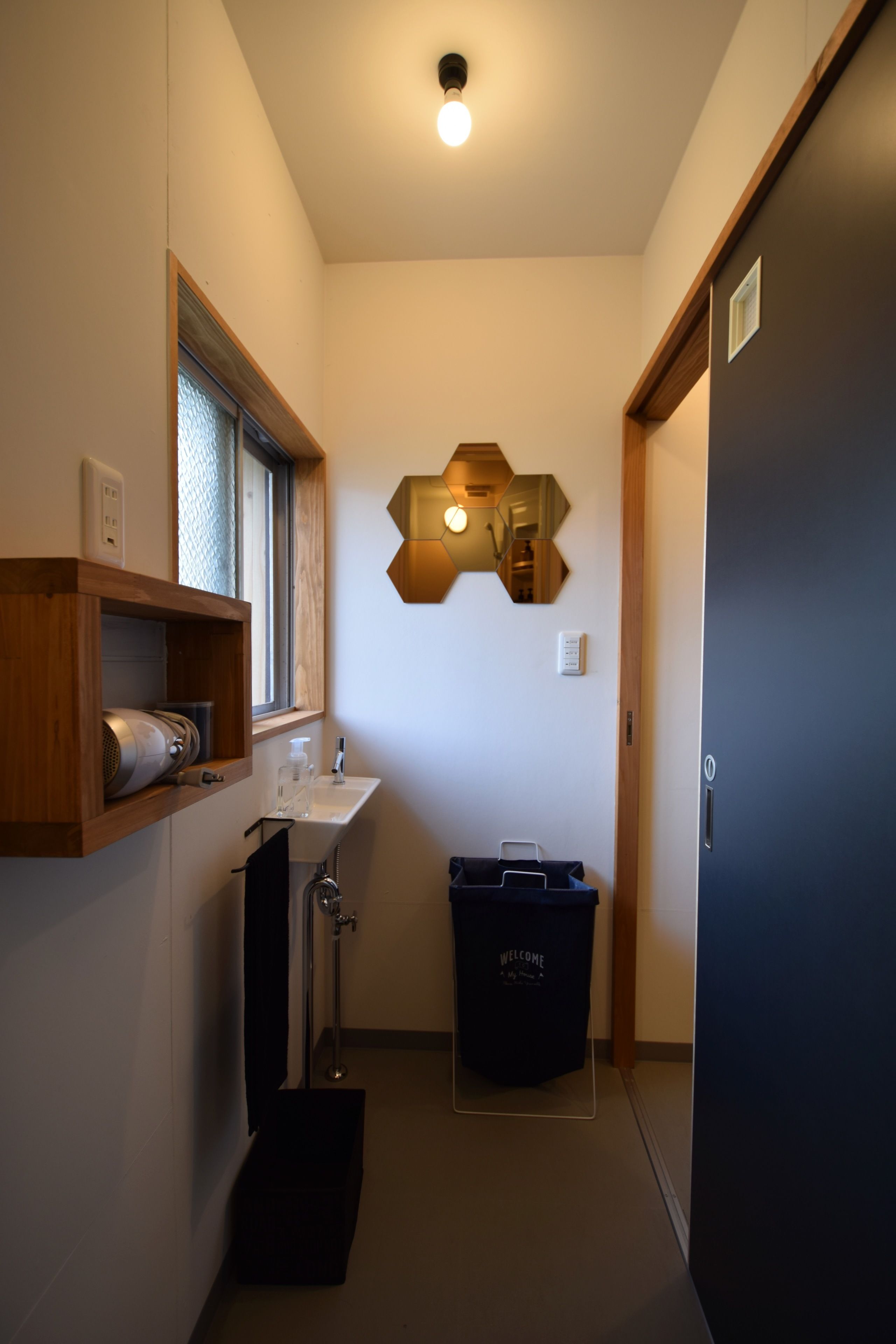 Un baño pequeño con ventana, un lavabo, toallero, ducha y un cubo de basura.