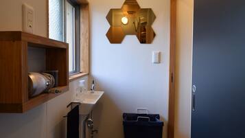 Un baño pequeño con ventana, un lavabo, toallero, ducha y un cubo de basura.