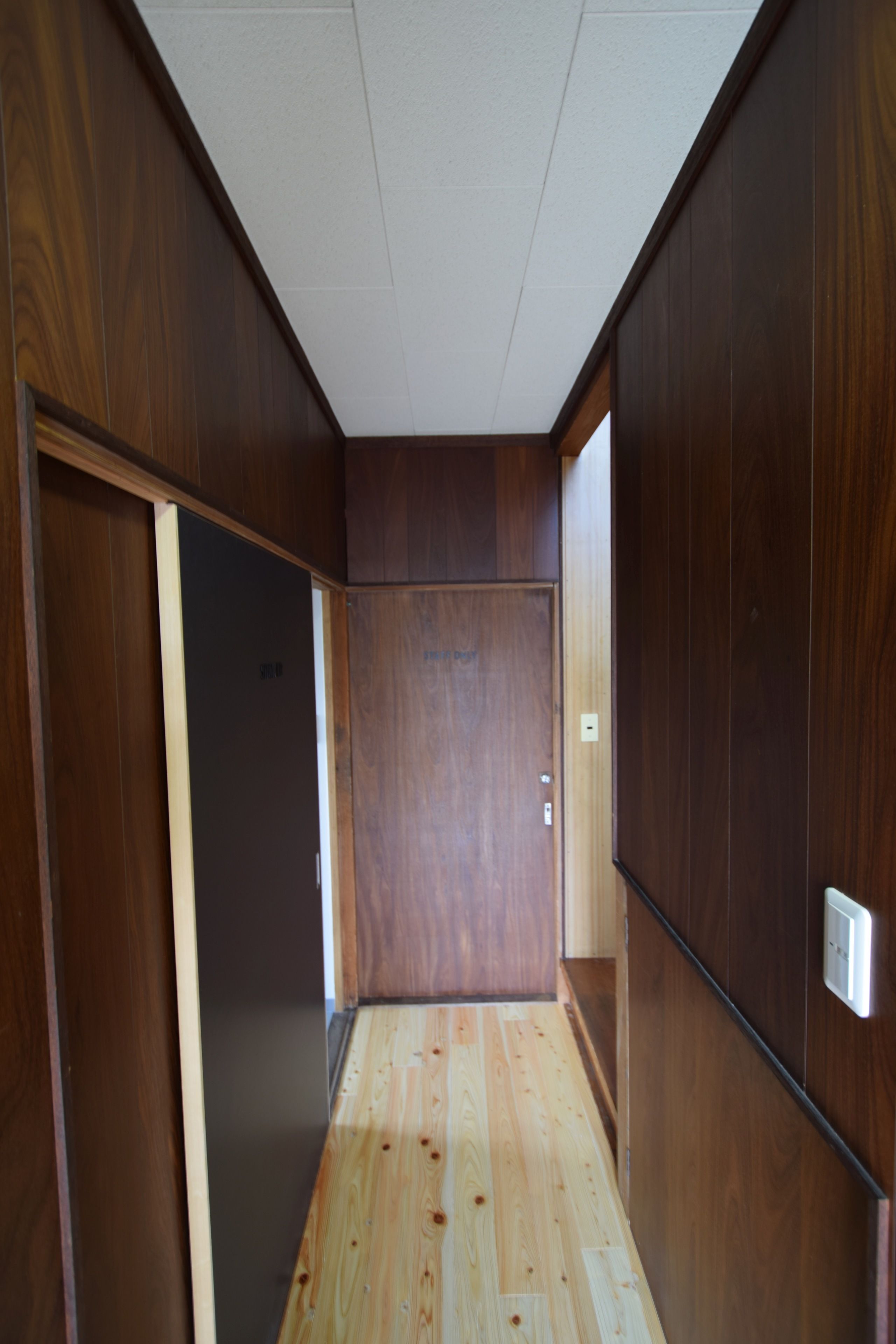 A narrow hallway with wooden walls and a wooden floor, leading to a door at the end.