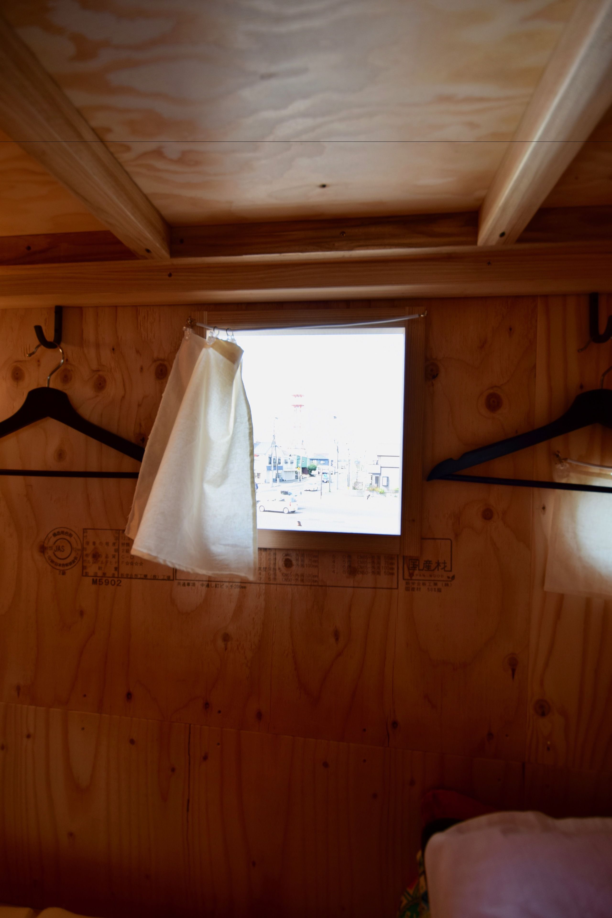 A small wooden room with a window, a hanging white cloth, and a black hanger.