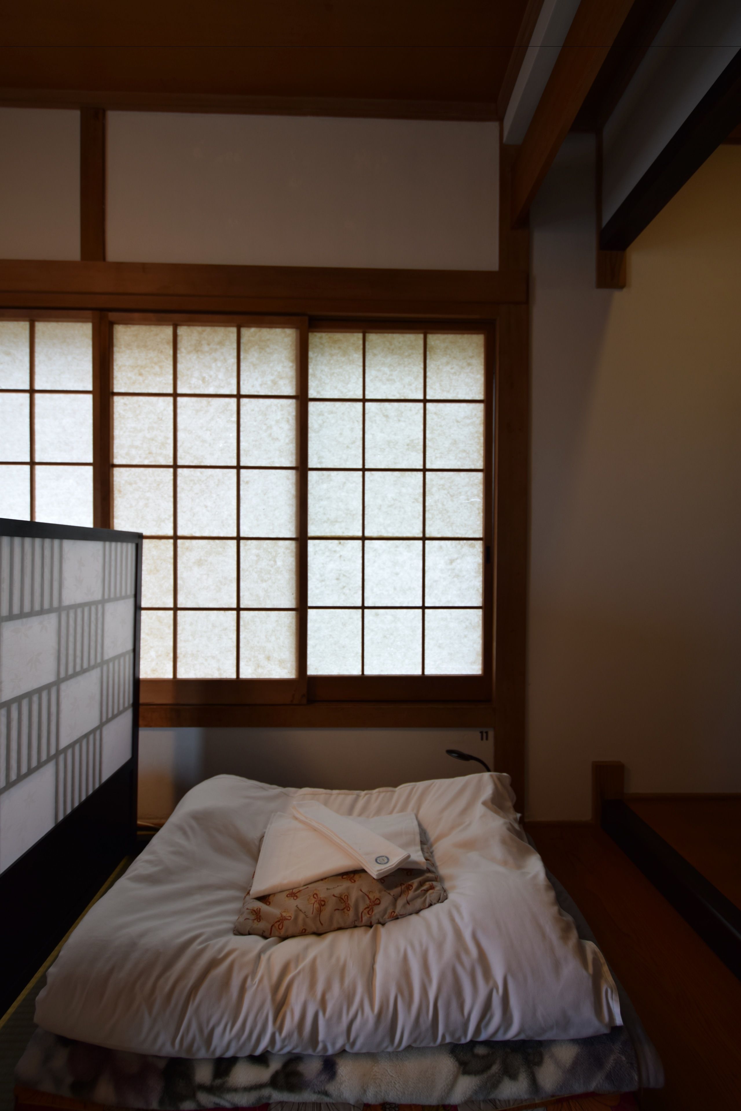 A traditional Japanese-style room with tatami flooring, a low wooden bed, and shoji screens.